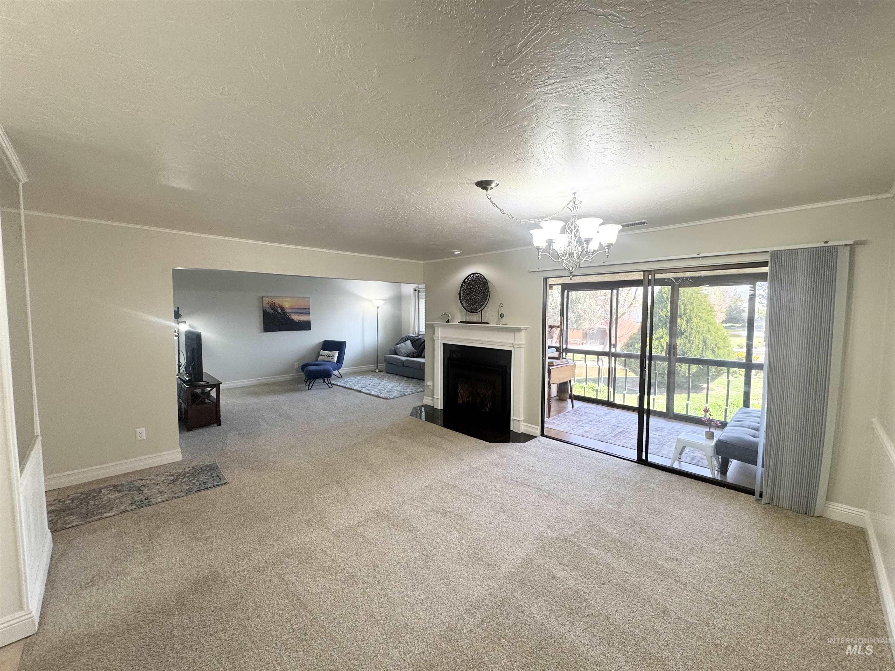 Unfurnished living room with suspended lighting, light colored carpet, a textured ceiling, and a fireplace with flush hearth