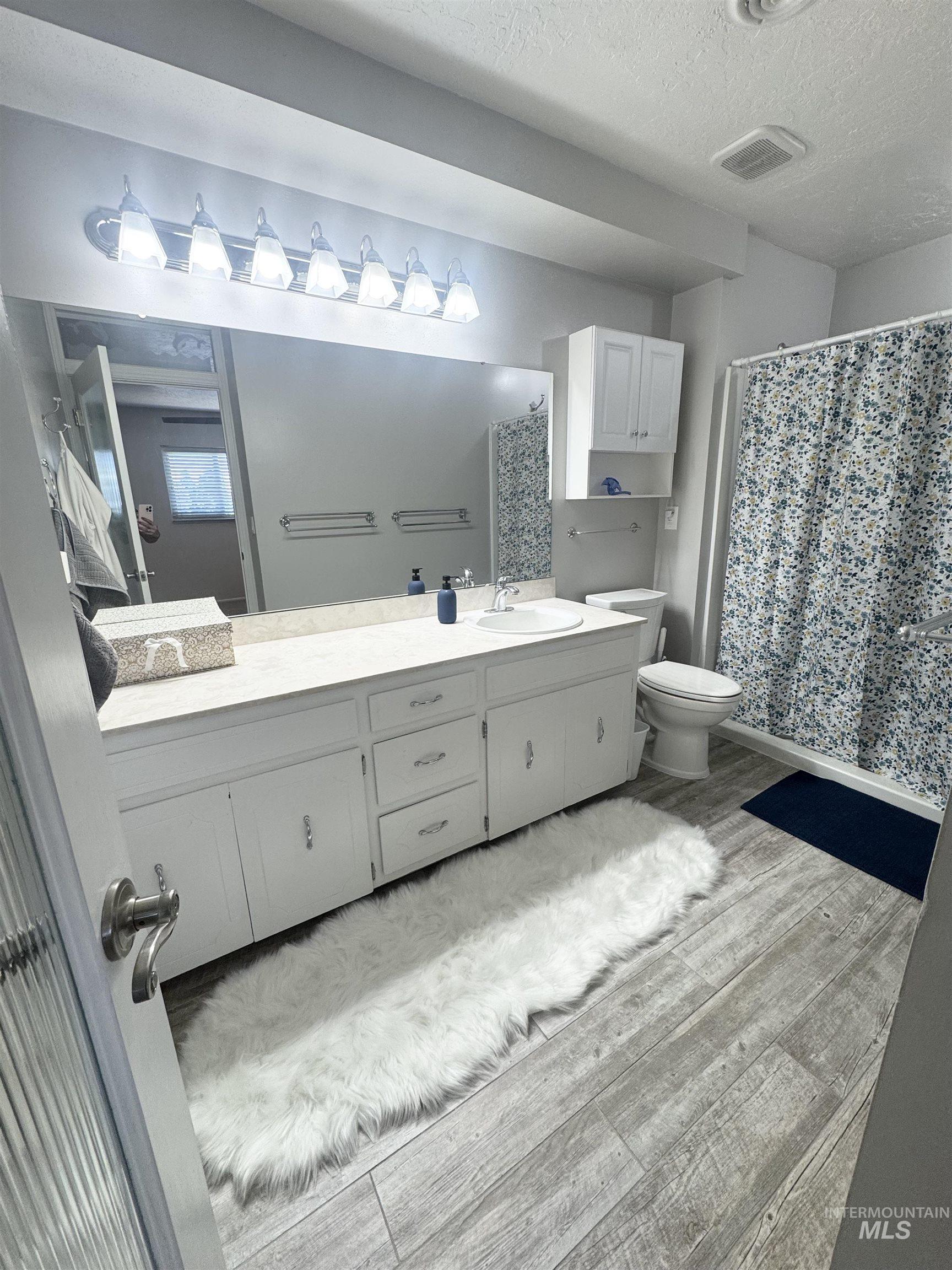 Full bathroom featuring vanity, curtained shower, light wood-style floors, and a textured ceiling