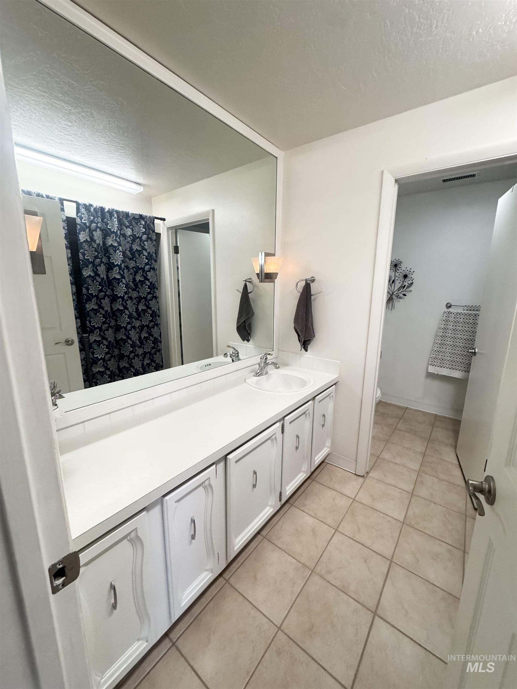 Full bath featuring a textured ceiling, vanity, a shower with shower curtain, and light tile patterned flooring