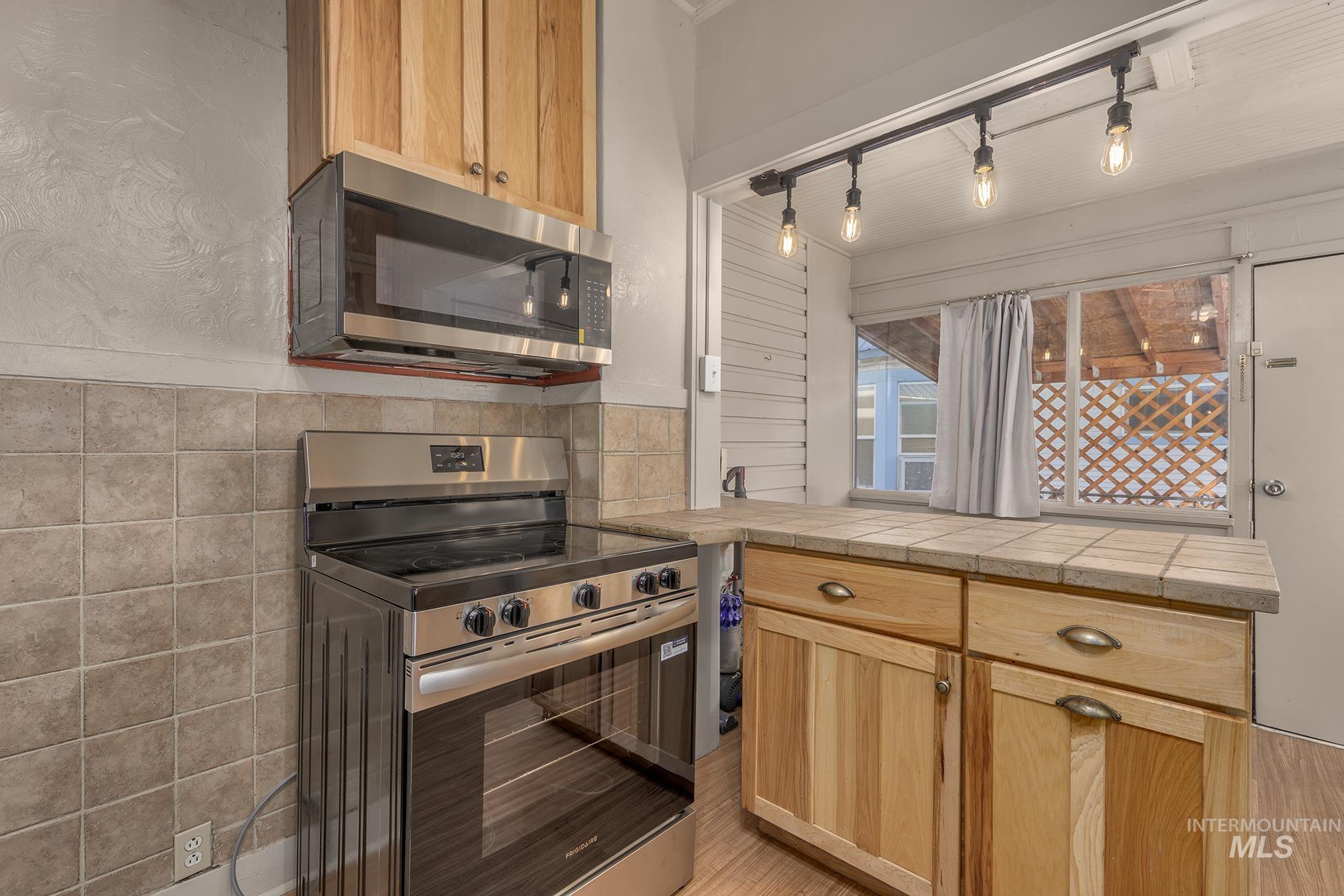 Kitchen with stainless steel appliances, light brown cabinets, track lighting, and a peninsula