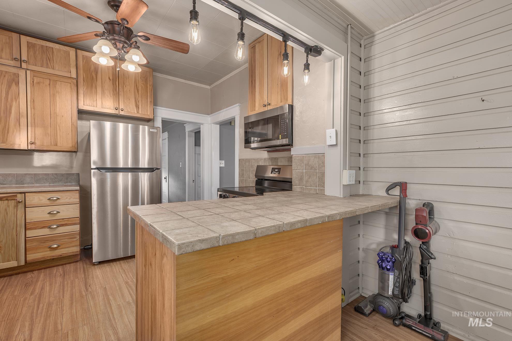 Kitchen with appliances with stainless steel finishes, a peninsula, hanging light fixtures, tile countertops, and crown molding