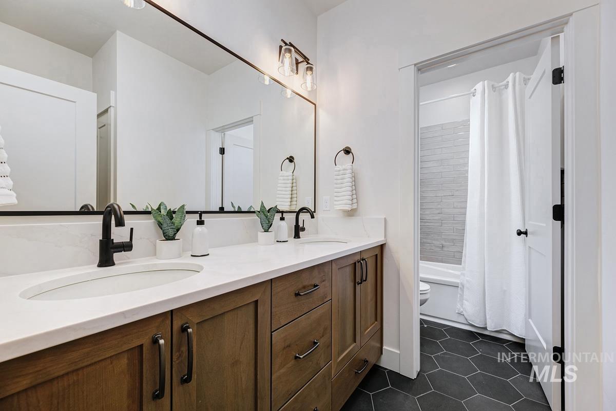 Full bathroom featuring double vanity, dark tile patterned flooring, and shower / bath combo with shower curtain