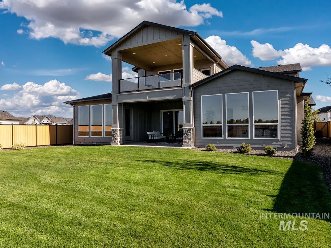 Rear view of house featuring board and batten siding, a patio area, a fenced backyard, a balcony, and stone siding