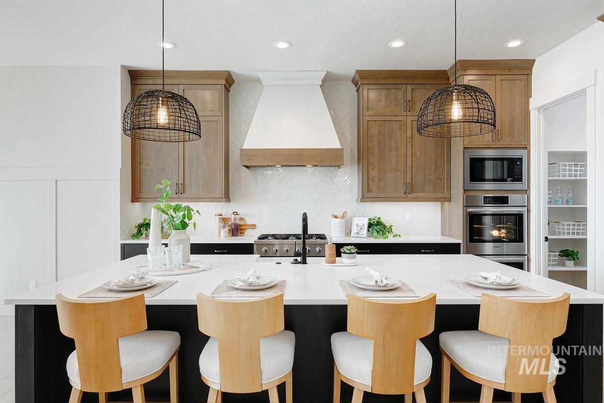 Kitchen featuring a breakfast bar area, a center island with sink, appliances with stainless steel finishes, light stone counters, and custom range hood