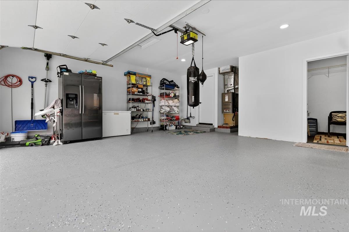 Garage featuring stainless steel refrigerator with ice dispenser, white refrigerator, a garage door opener, and heating unit