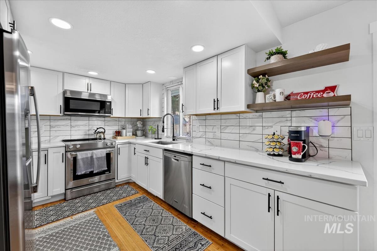 Kitchen with white cabinetry, light wood-style floors, stainless steel appliances, light stone countertops, and recessed lighting