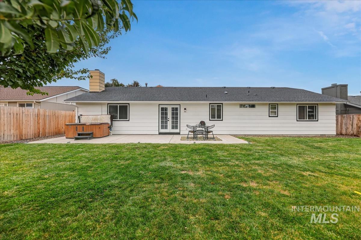 Rear view of property featuring a hot tub, a patio area, a fenced backyard, and french doors