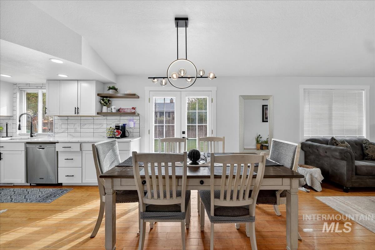 Dining space with light wood-style flooring, lofted ceiling, a chandelier, french doors, and recessed lighting