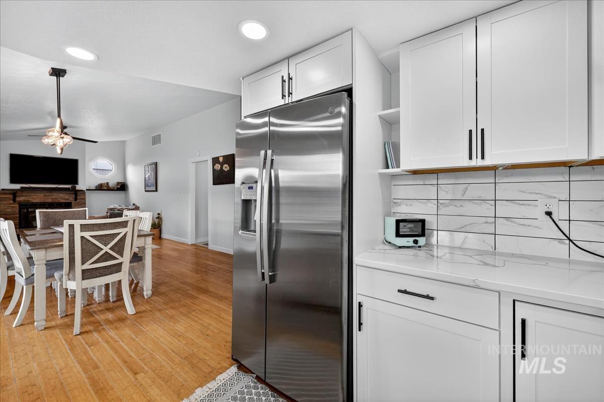 Kitchen featuring stainless steel fridge with ice dispenser, white cabinetry, light wood-style floors, decorative backsplash, and light stone counters
