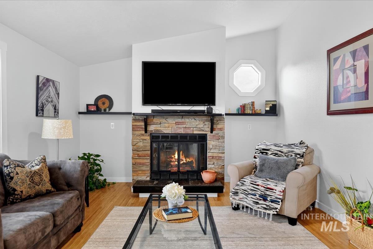 Living room with wood finished floors, a stone fireplace, and lofted ceiling