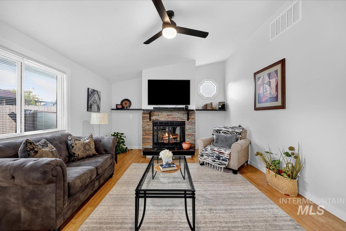 Living area featuring lofted ceiling, light wood-type flooring, a fireplace, and ceiling fan