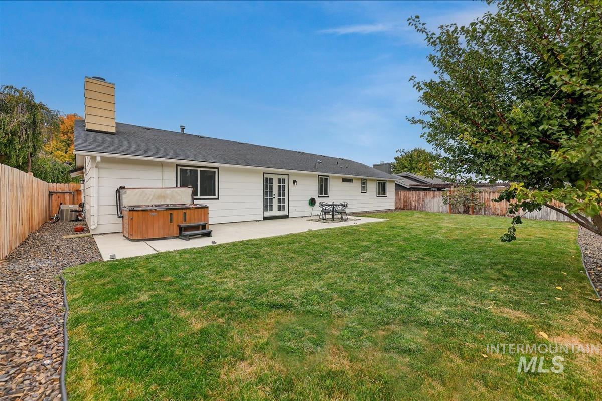 Rear view of house featuring a hot tub, a fenced backyard, a chimney, a patio, and french doors