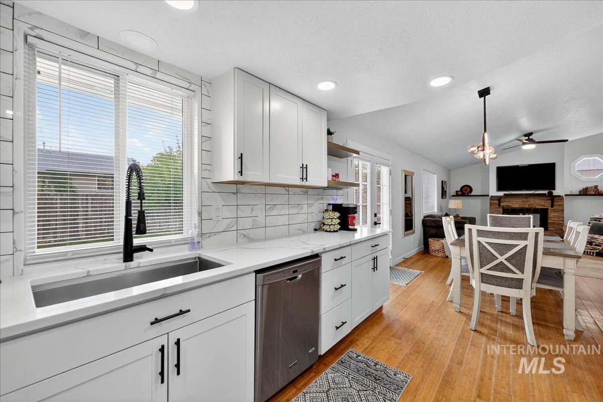 Kitchen with white cabinetry, decorative light fixtures, tasteful backsplash, dishwasher, and lofted ceiling