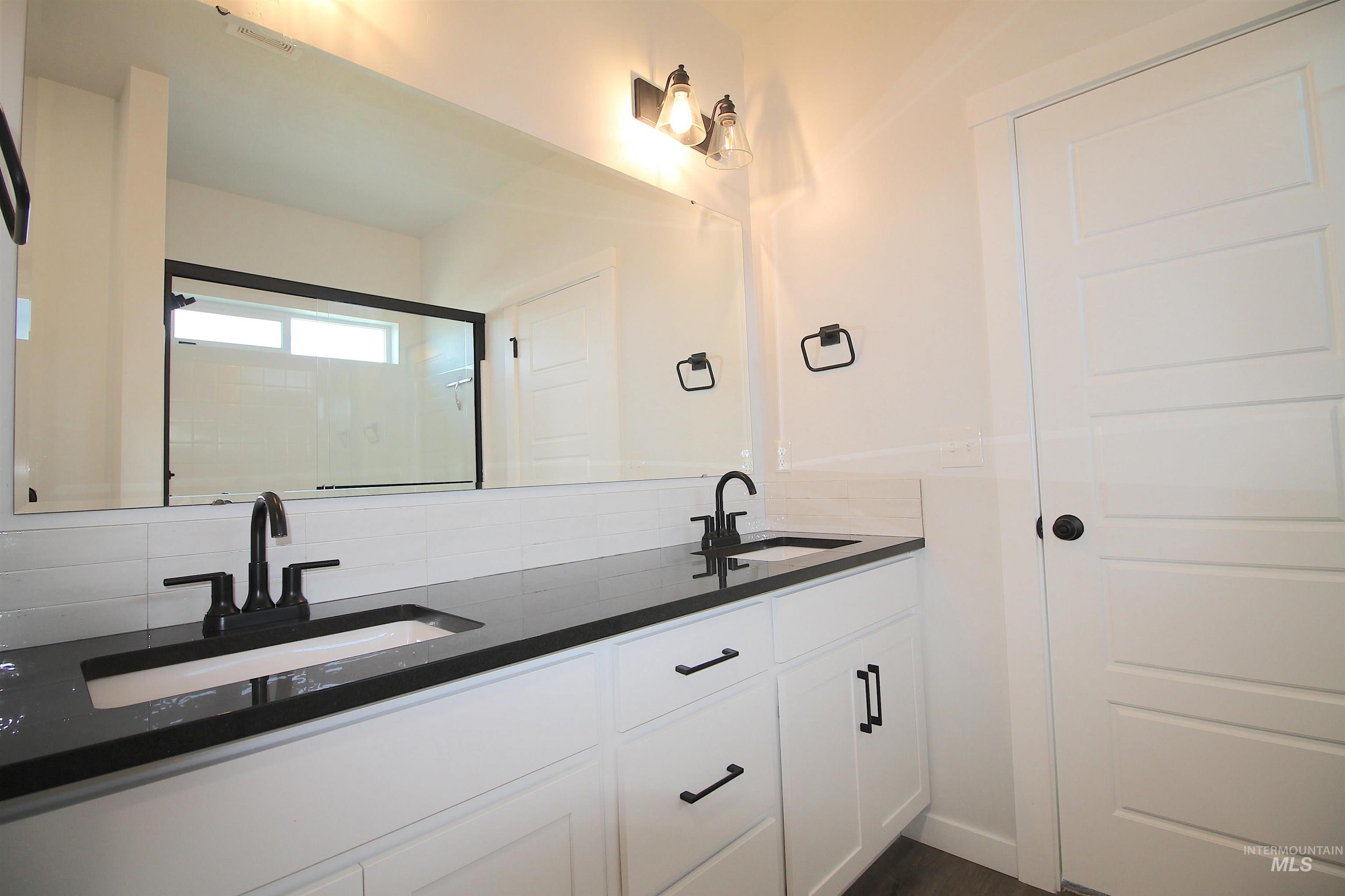 Dual vanity with matte black fixtures, integrated sinks, dark countertops, and white shaker-style cabinetry