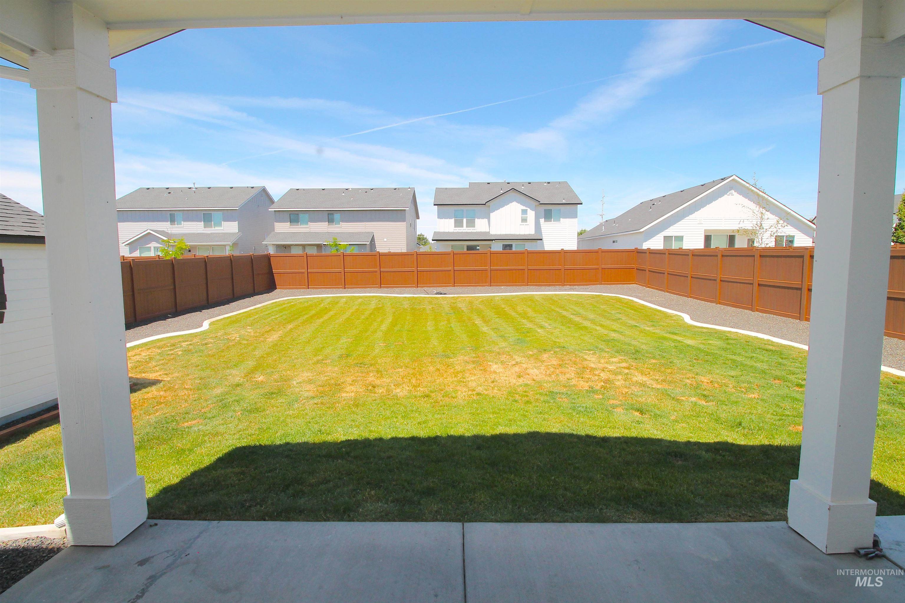 Expansive backyard featuring a manicured lawn, a brown privacy fence, and a concrete patio