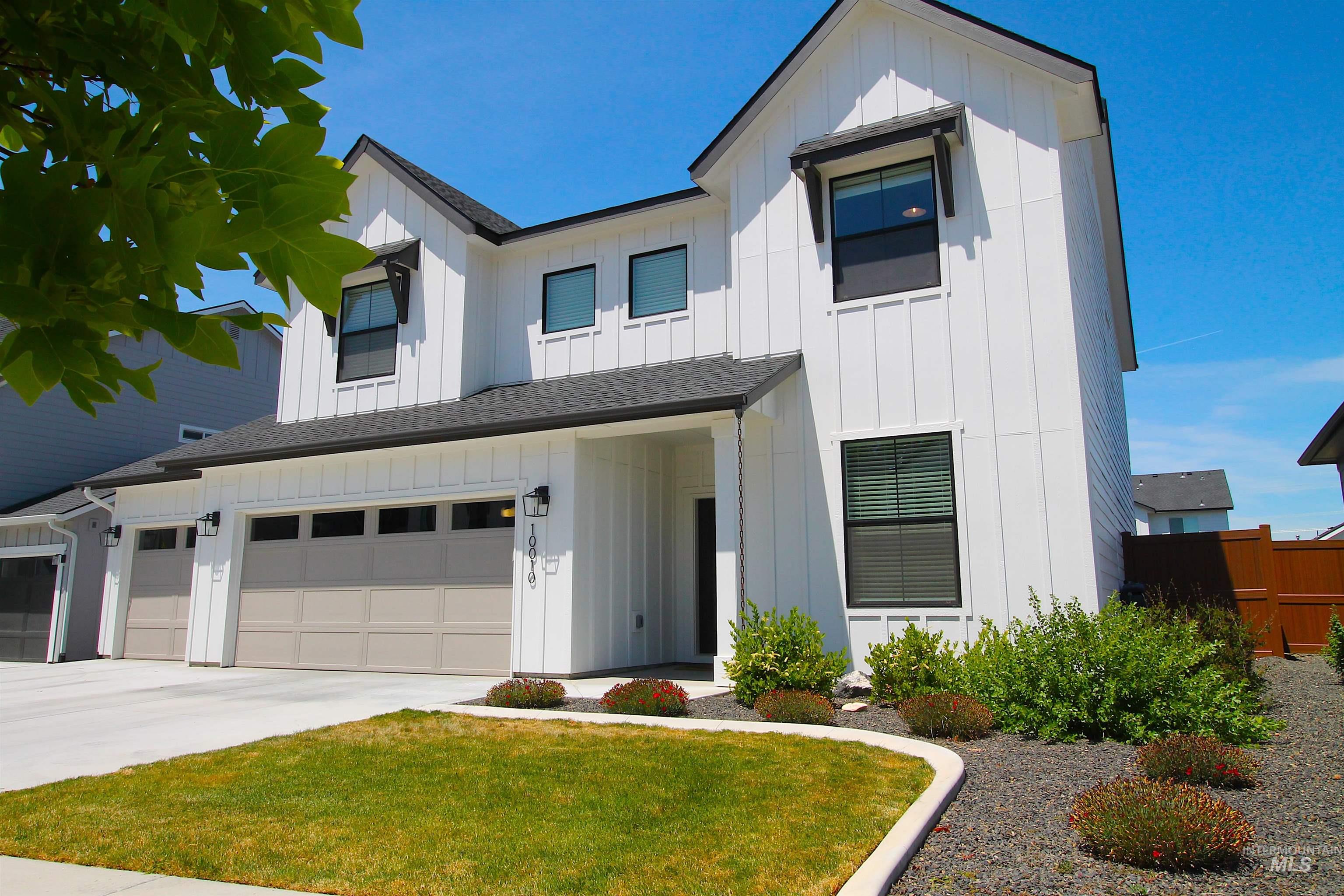 Modern farmhouse exterior featuring white vertical siding, black trim windows, an attached two-car garage with light gray doors, and a dark shingle roof