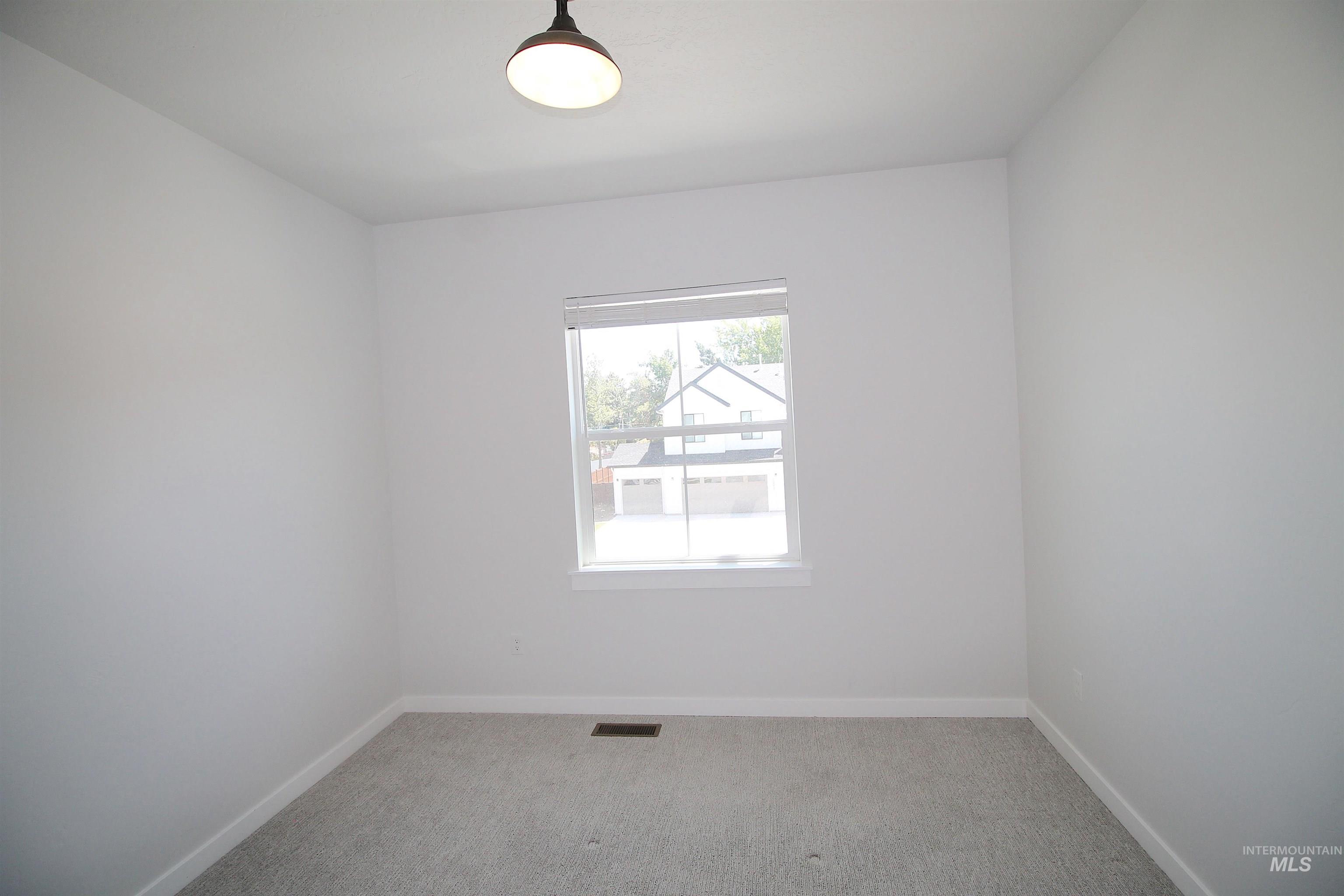 Bright interior room featuring a window with white trim, a flush-mount light fixture, and light grey carpet