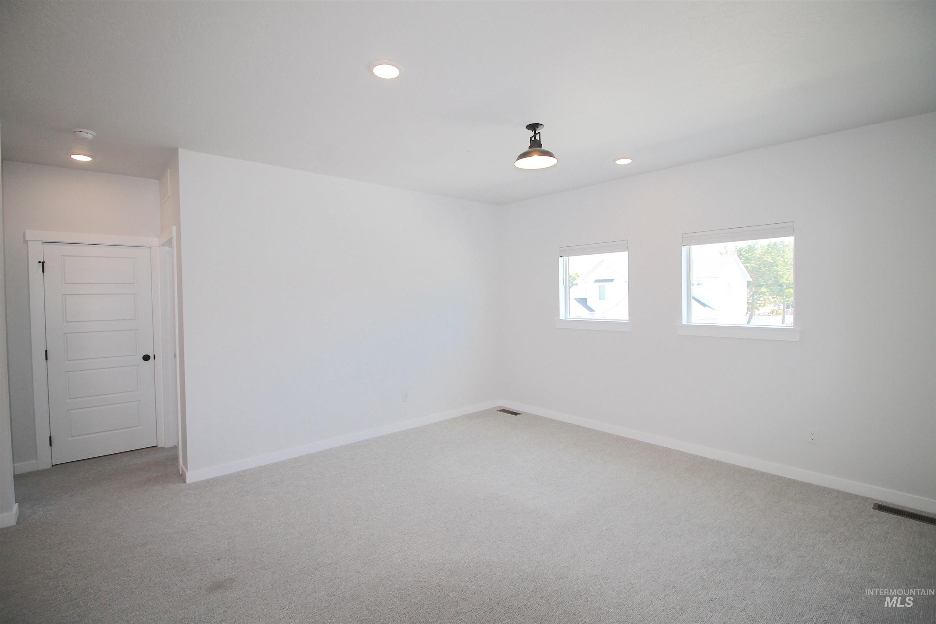 Spacious room featuring light gray carpeting, crisp white walls, two windows, recessed lighting, and a modern ceiling light fixture