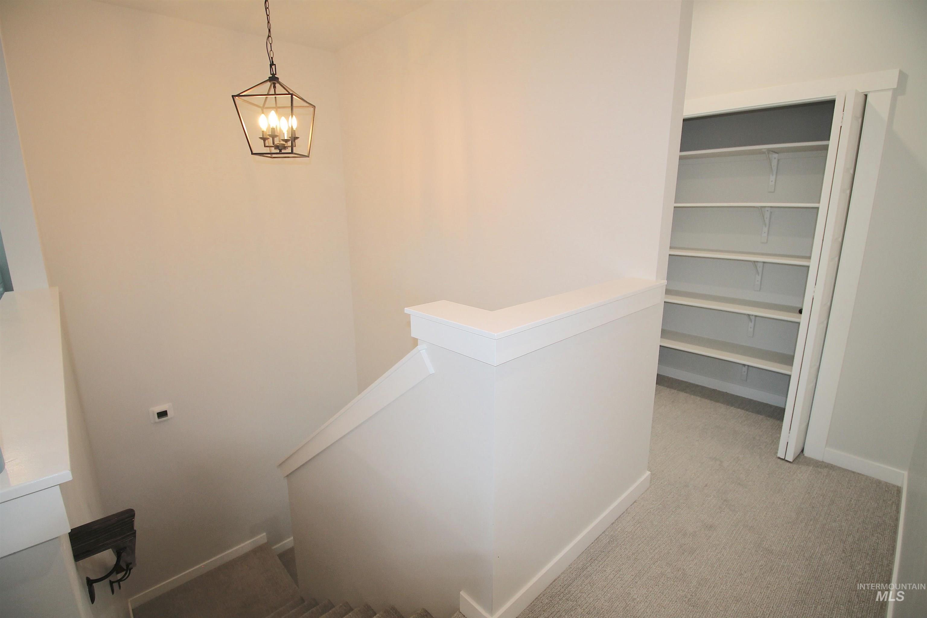 Carpeted staircase with white trim, a geometric pendant light fixture, and an adjacent built-in shelving unit