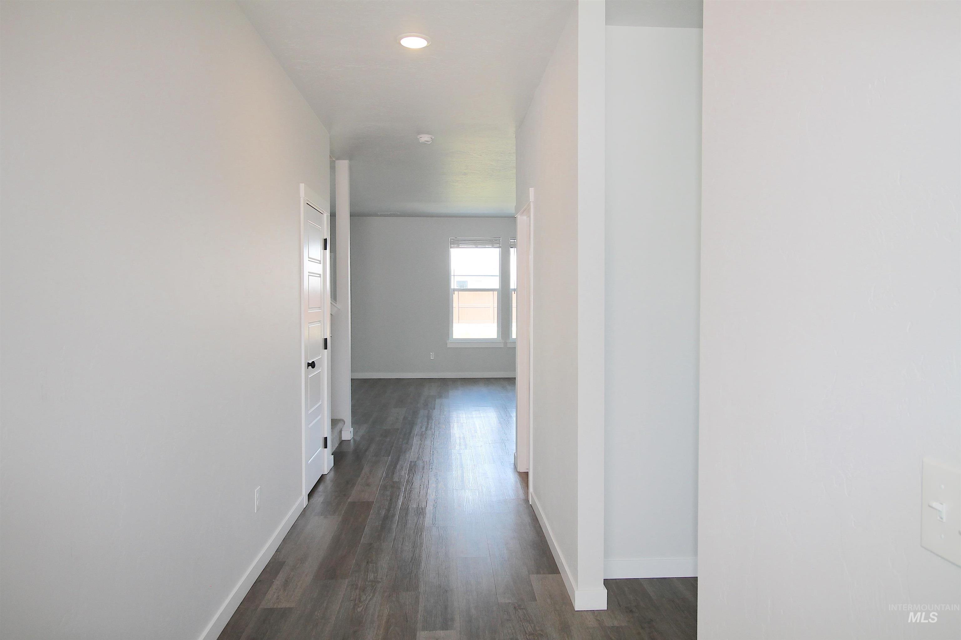 Hallway featuring wood-finish flooring, recessed lighting, white trim, and a paneled interior door with a black handle