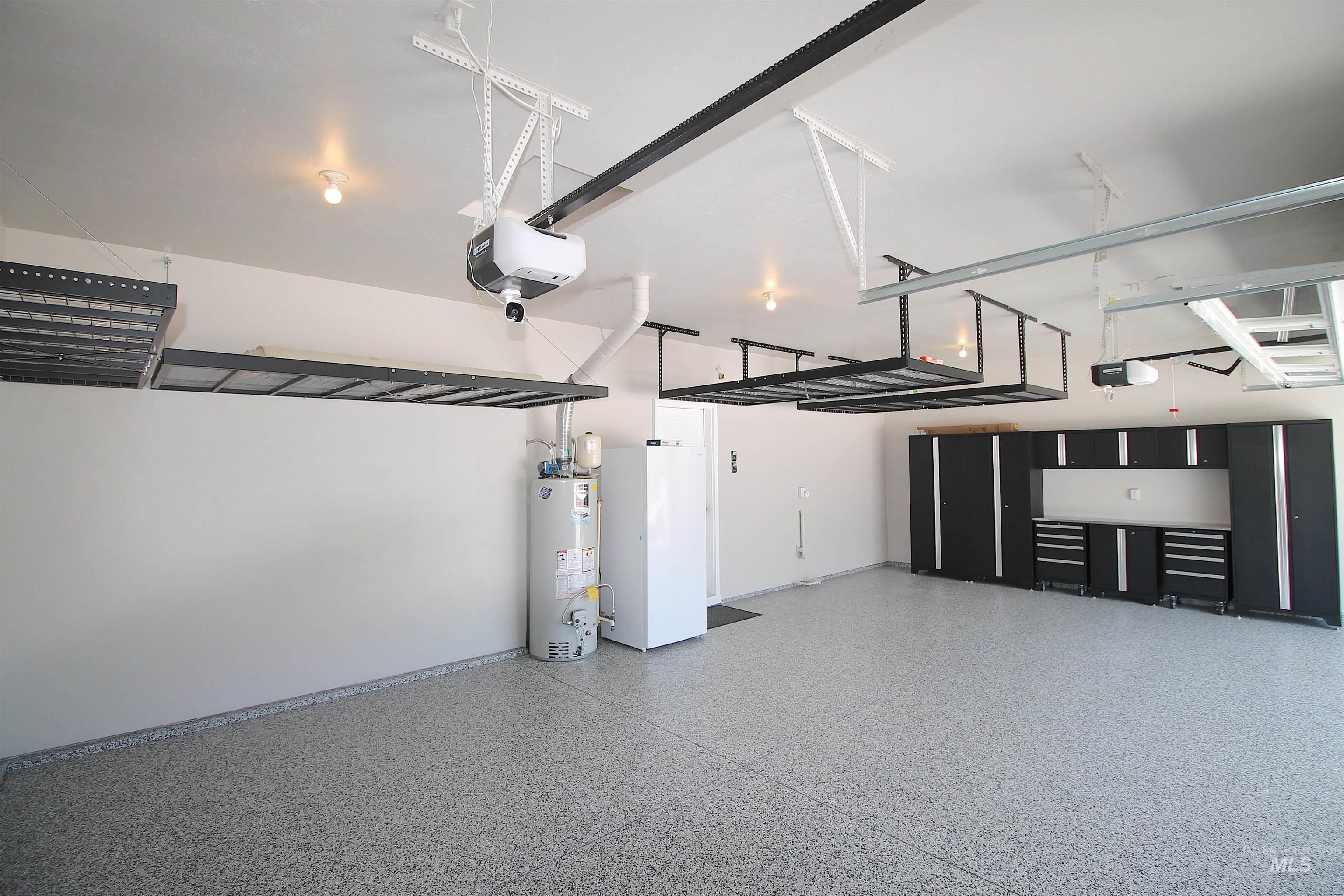 Spacious garage featuring an epoxy floor, extensive built-in cabinetry, overhead storage racks, and ceiling-mounted lighting