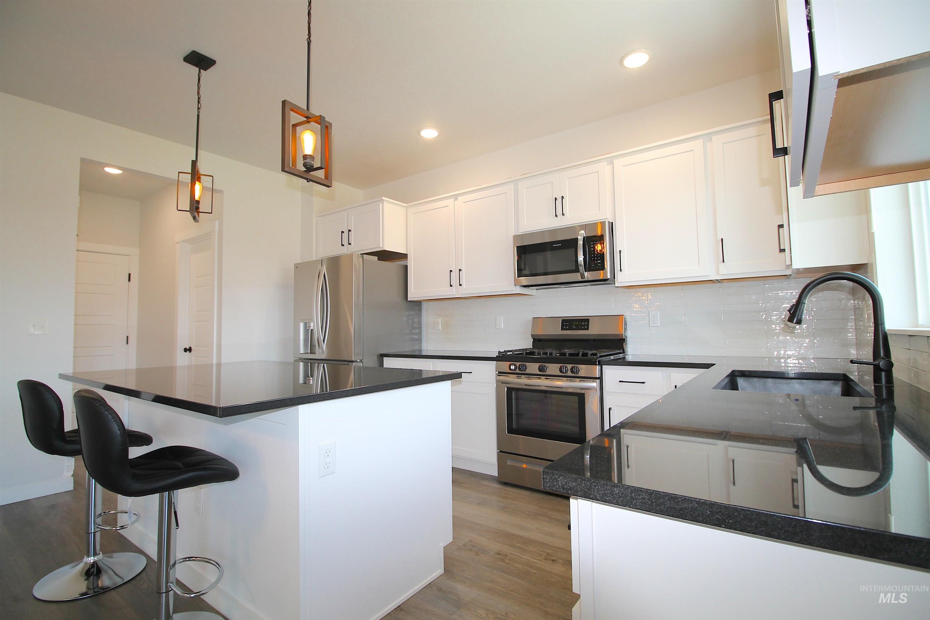 Kitchen featuring white cabinetry, dark countertops, stainless steel appliances, a white subway tile backsplash, and wood-finish flooring