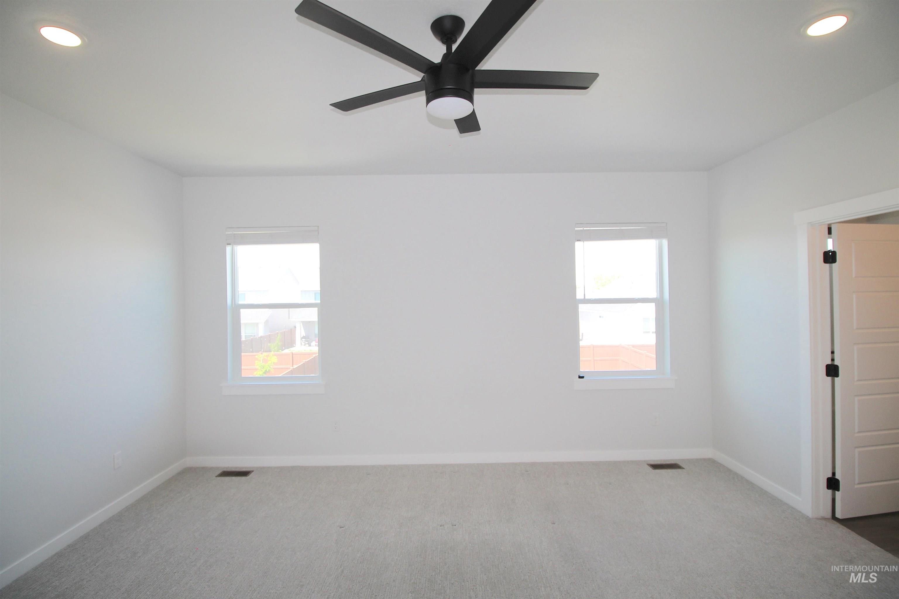 Room featuring light gray carpet flooring, two windows, recessed ceiling lighting, and a modern black ceiling fan
