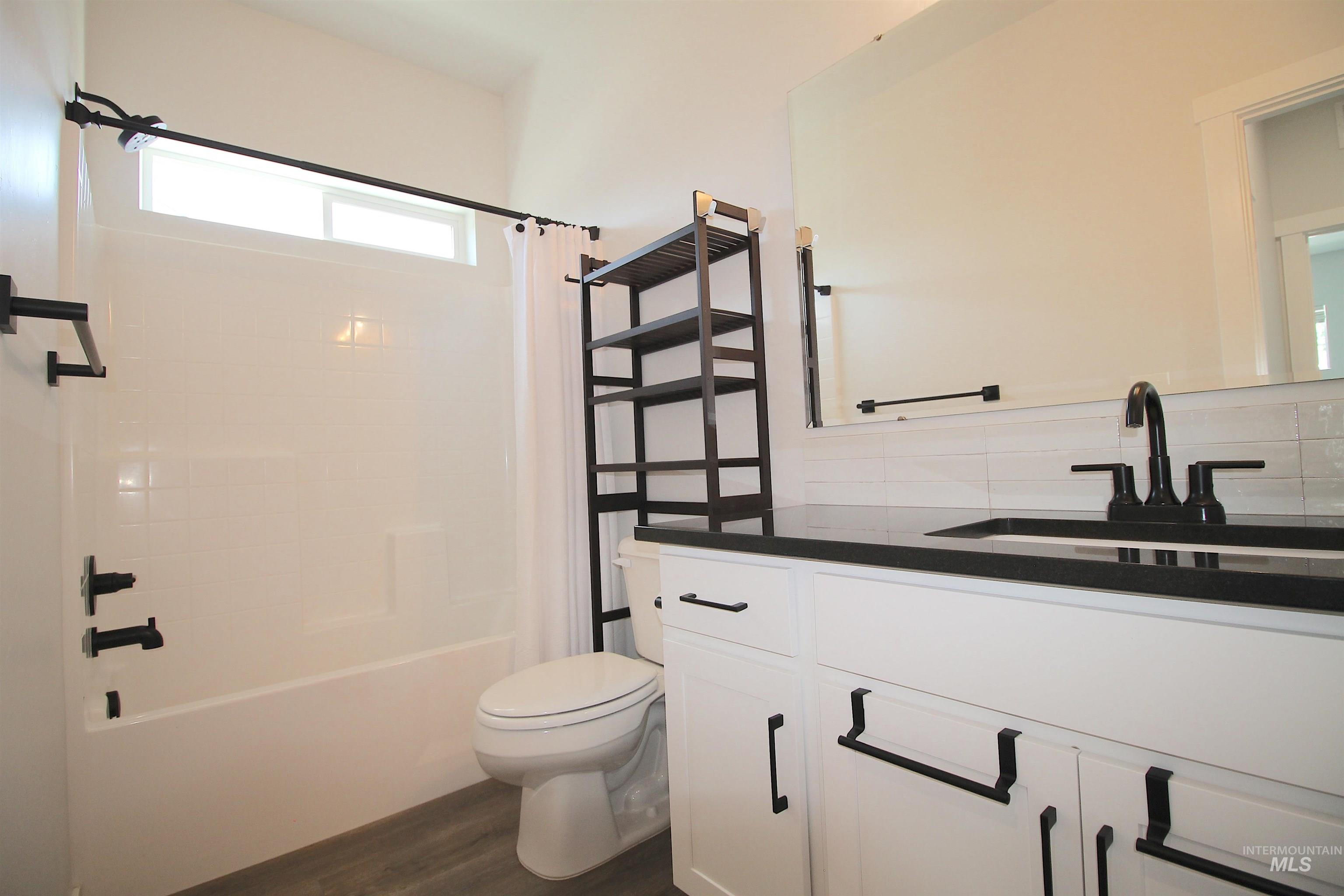 Bathroom featuring white vanity cabinetry, dark countertop, black fixtures, and wood-finish flooring