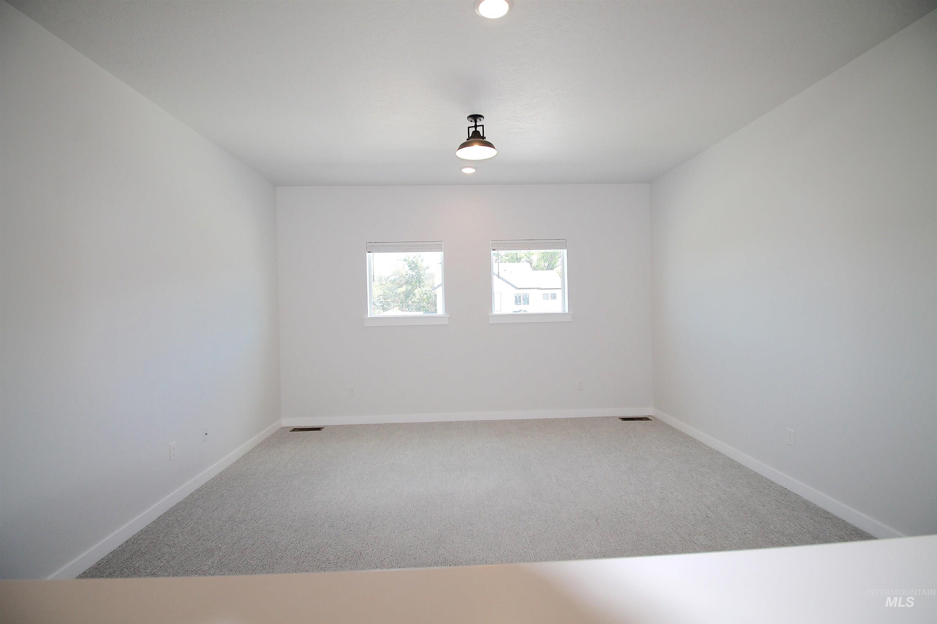 Spacious room featuring light-colored carpeting, white walls, and a contemporary ceiling light fixture