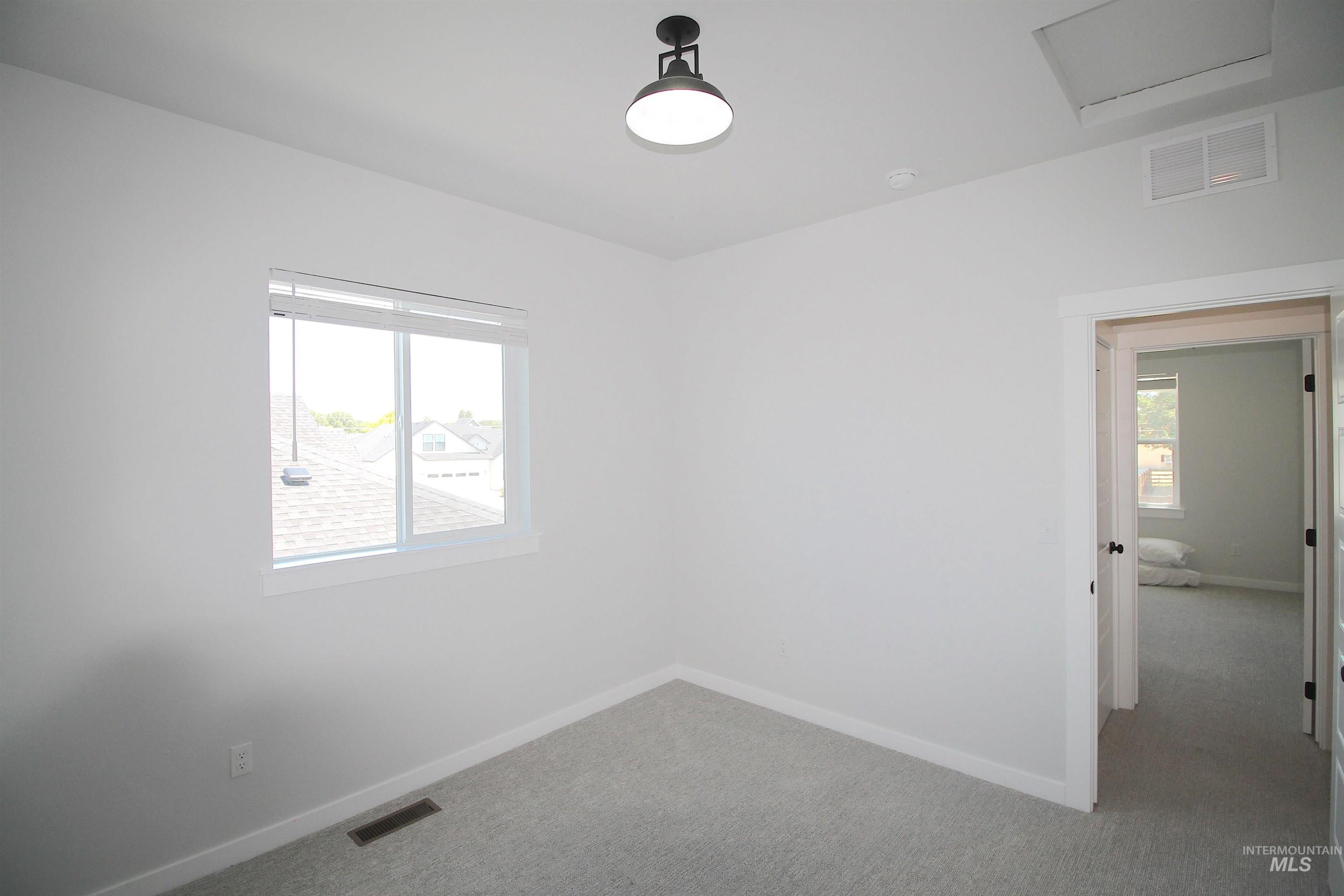 Room featuring light gray carpeting, crisp white walls, a double-pane window, and a matte black flush mount ceiling light fixture