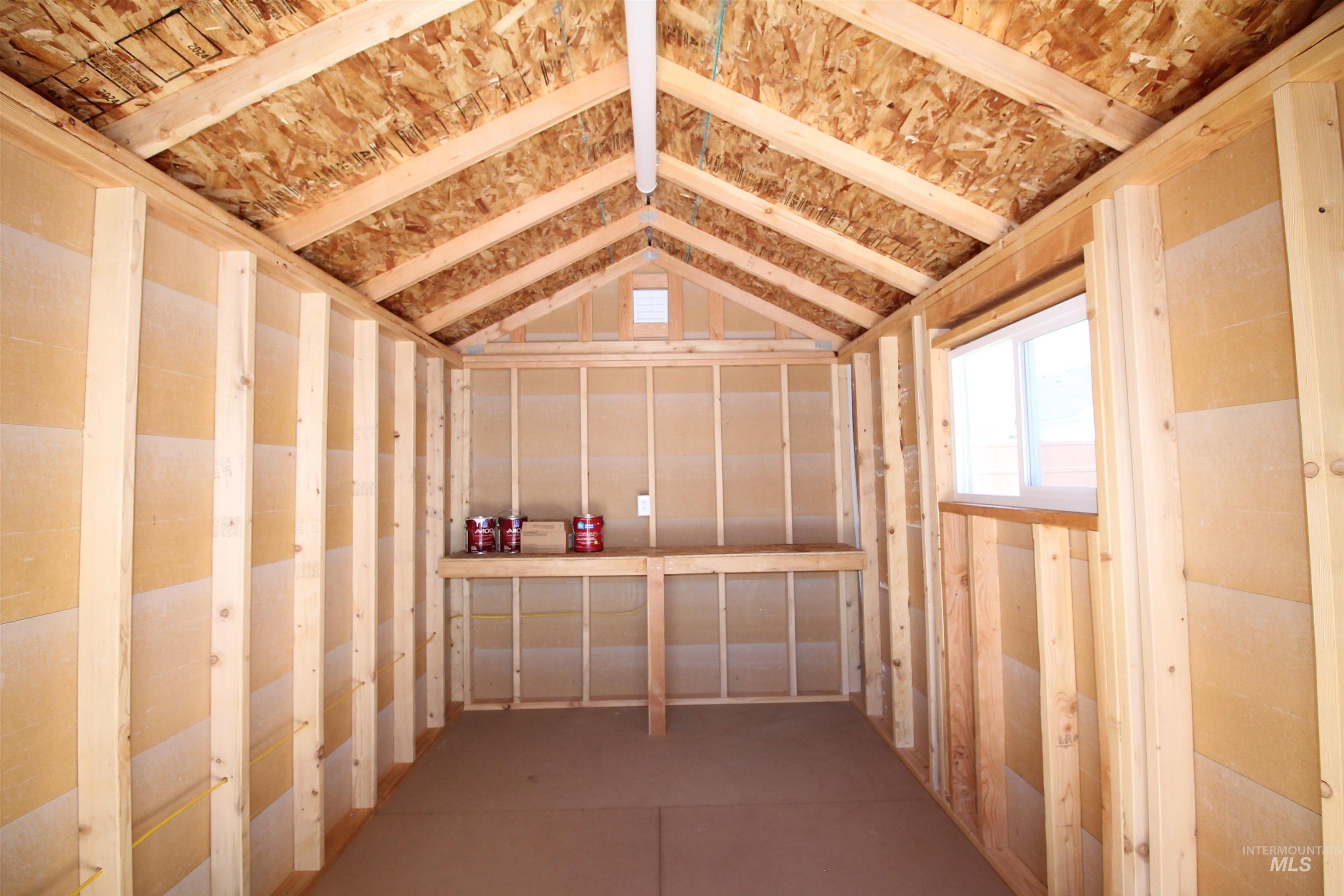 Interior of a utility structure featuring exposed wood framing, an open-rafter ceiling with oriented strand board, a built-in workbench, and a single window