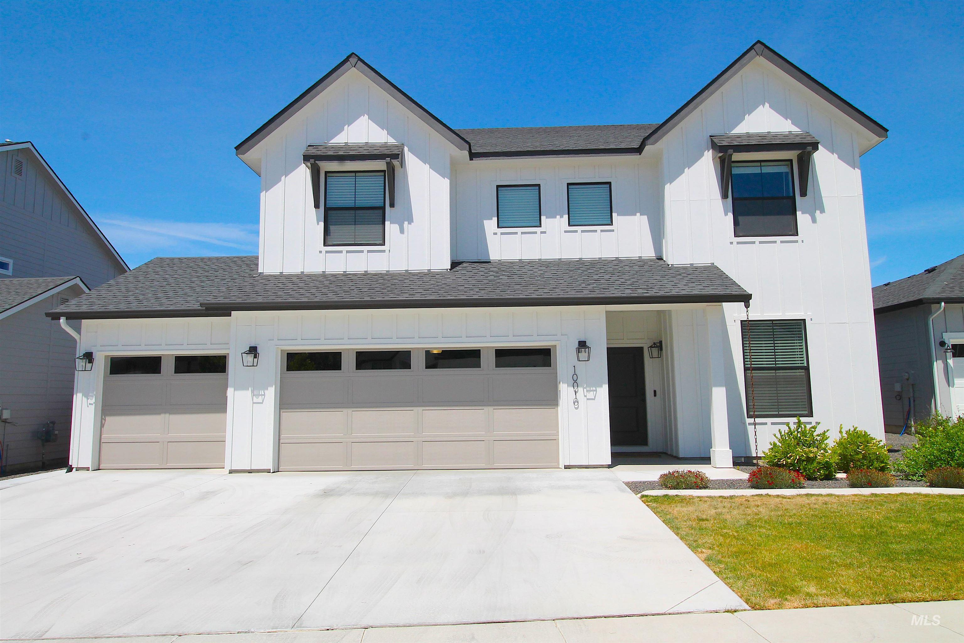 Contemporary farmhouse exterior featuring white vertical siding, dark trim windows, a two-car garage, an additional single-car garage, and a covered entry