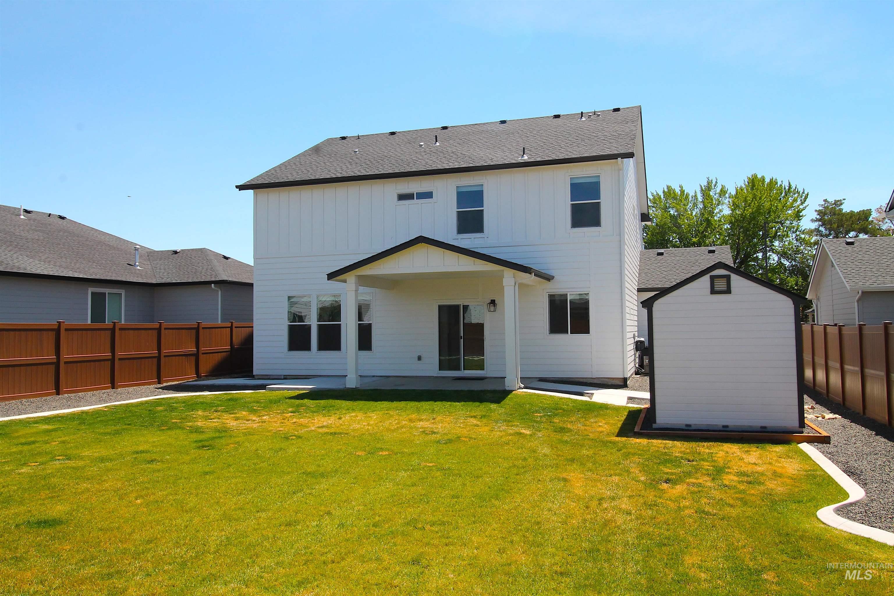 Expansive backyard featuring a manicured lawn, a covered patio, and a storage shed with a contrasting dark trim