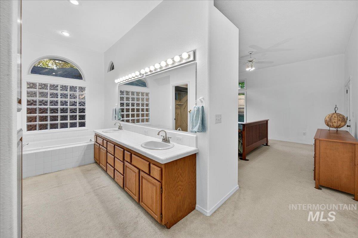 Full bathroom featuring light colored carpet, double vanity, healthy amount of natural light, and a ceiling fan