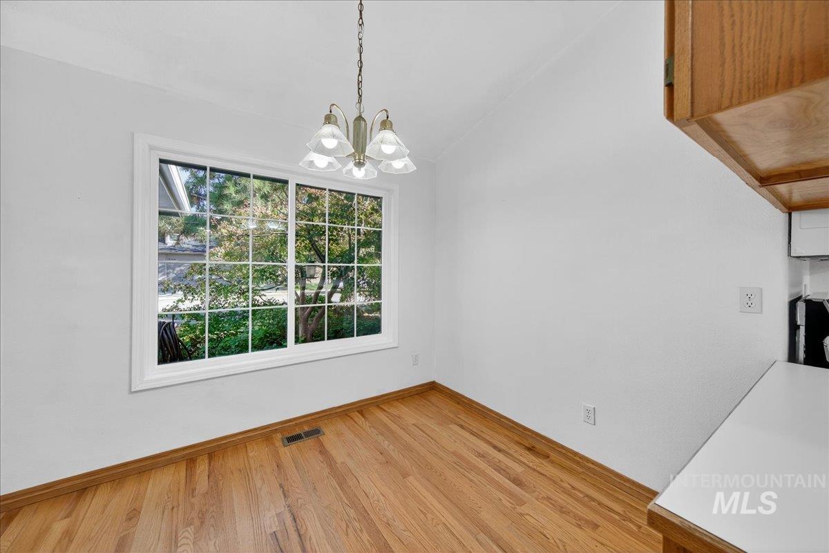 Unfurnished dining area with light wood-style flooring, vaulted ceiling, and a chandelier