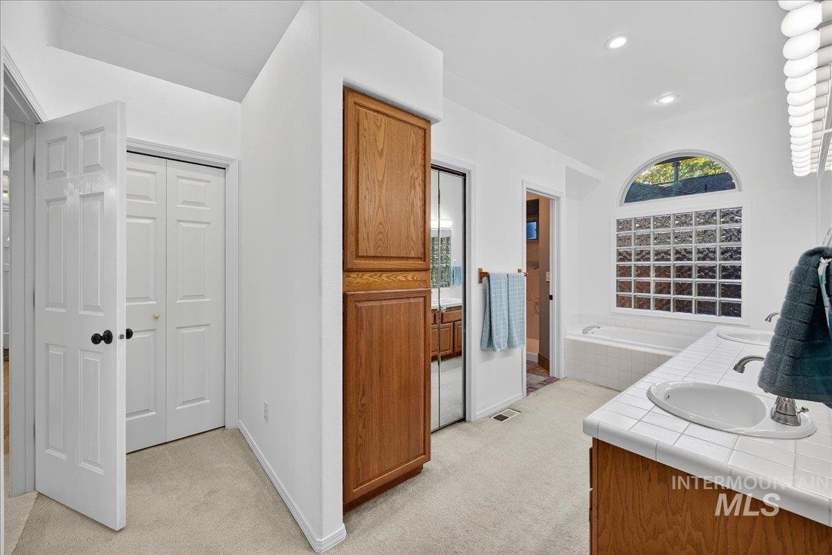 Bathroom featuring light carpet, a bath, double vanity, and recessed lighting