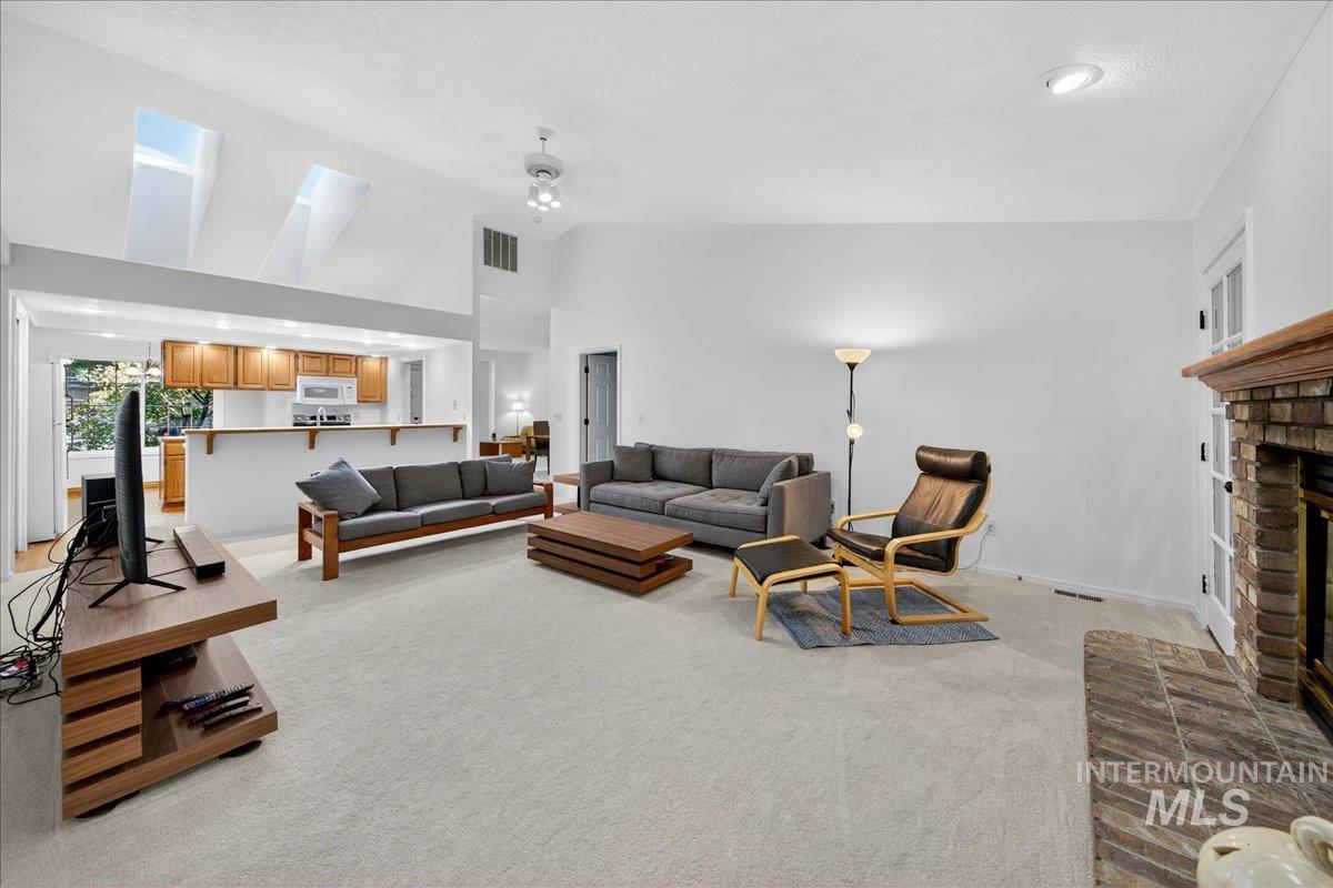 Living area featuring light carpet, a brick fireplace, and a towering ceiling