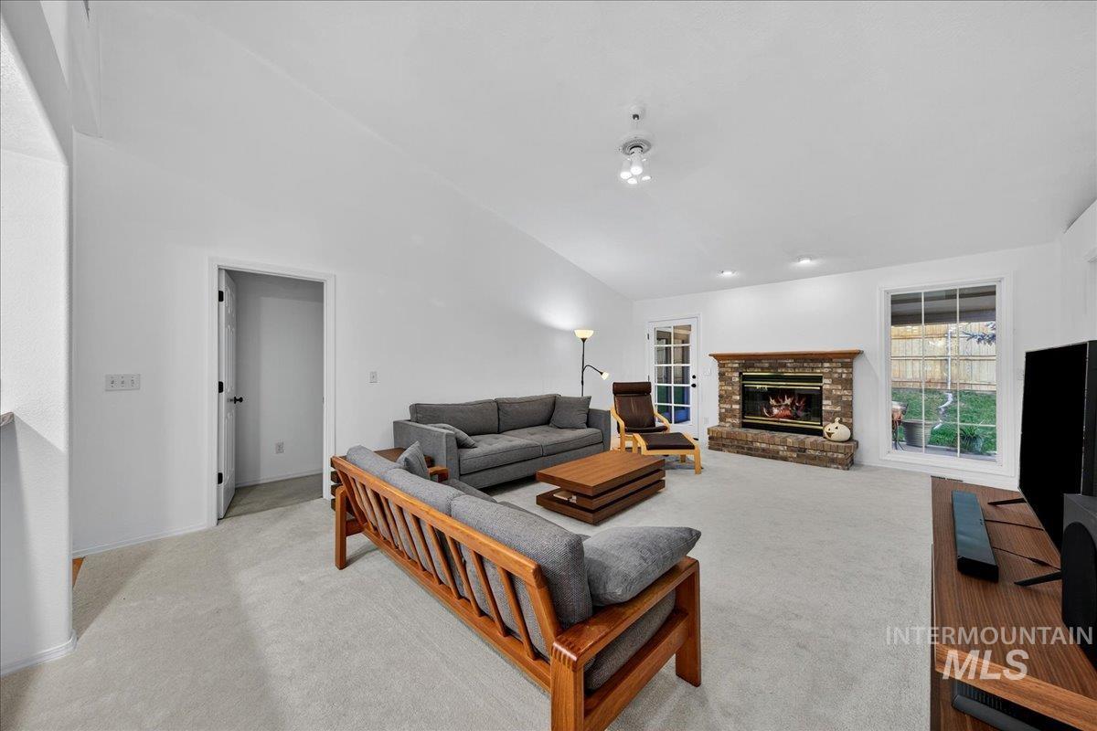 Carpeted living room with vaulted ceiling and a brick fireplace