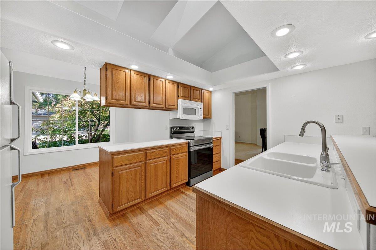 Kitchen with light countertops, stainless steel appliances, brown cabinets, a chandelier, and recessed lighting