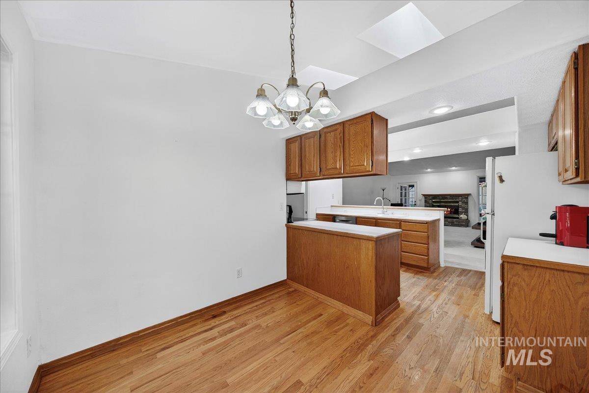 Kitchen featuring brown cabinetry, a peninsula, light countertops, light wood-type flooring, and a chandelier