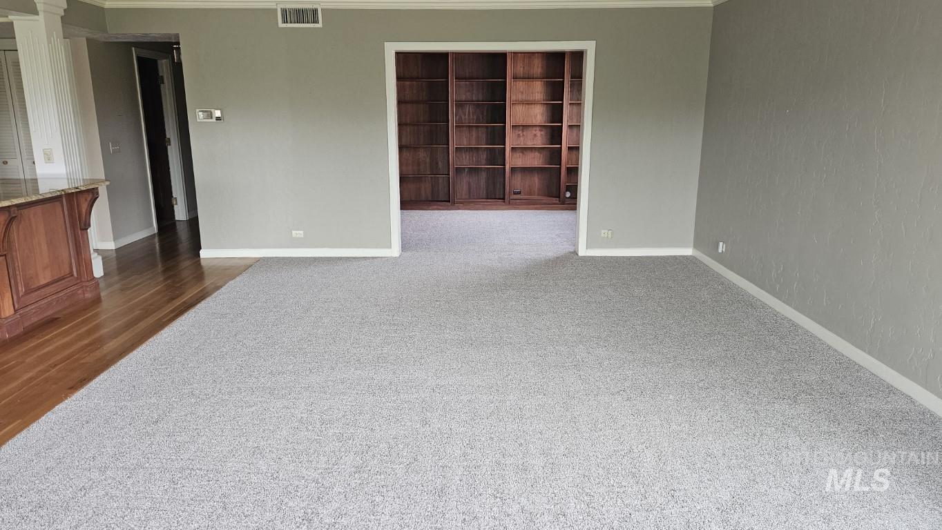 Empty room with crown molding, dark colored carpet, and dark wood-style floors