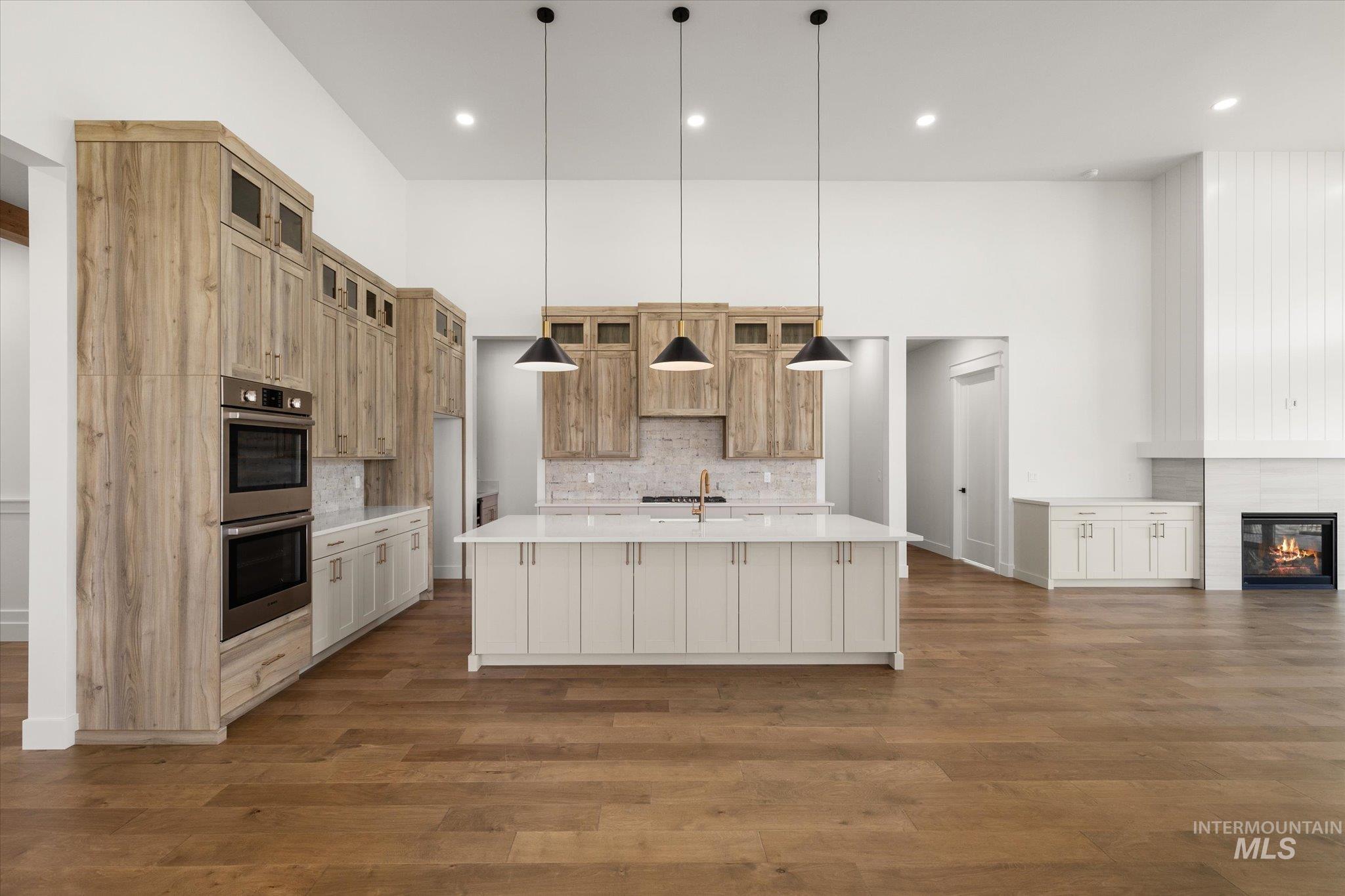 Kitchen with a large island, backsplash, decorative light fixtures, dark wood-style floors, and stainless steel double oven