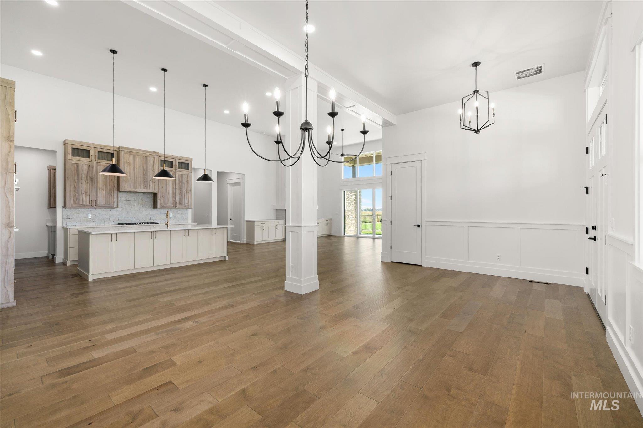 Unfurnished living room featuring a chandelier, dark wood finished floors, a high ceiling, and a wainscoted wall
