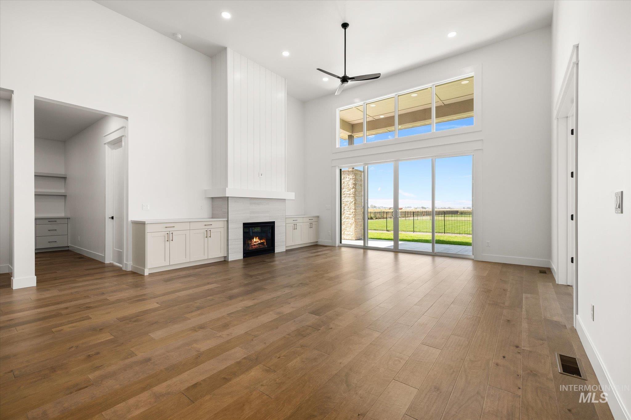 Unfurnished living room with a high ceiling, light wood-type flooring, ceiling fan, a tiled fireplace, and recessed lighting