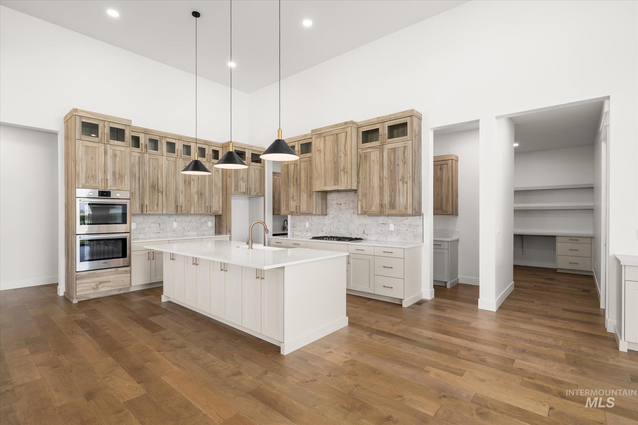 Kitchen with stainless steel double oven, a kitchen island with sink, tasteful backsplash, glass insert cabinets, and a towering ceiling