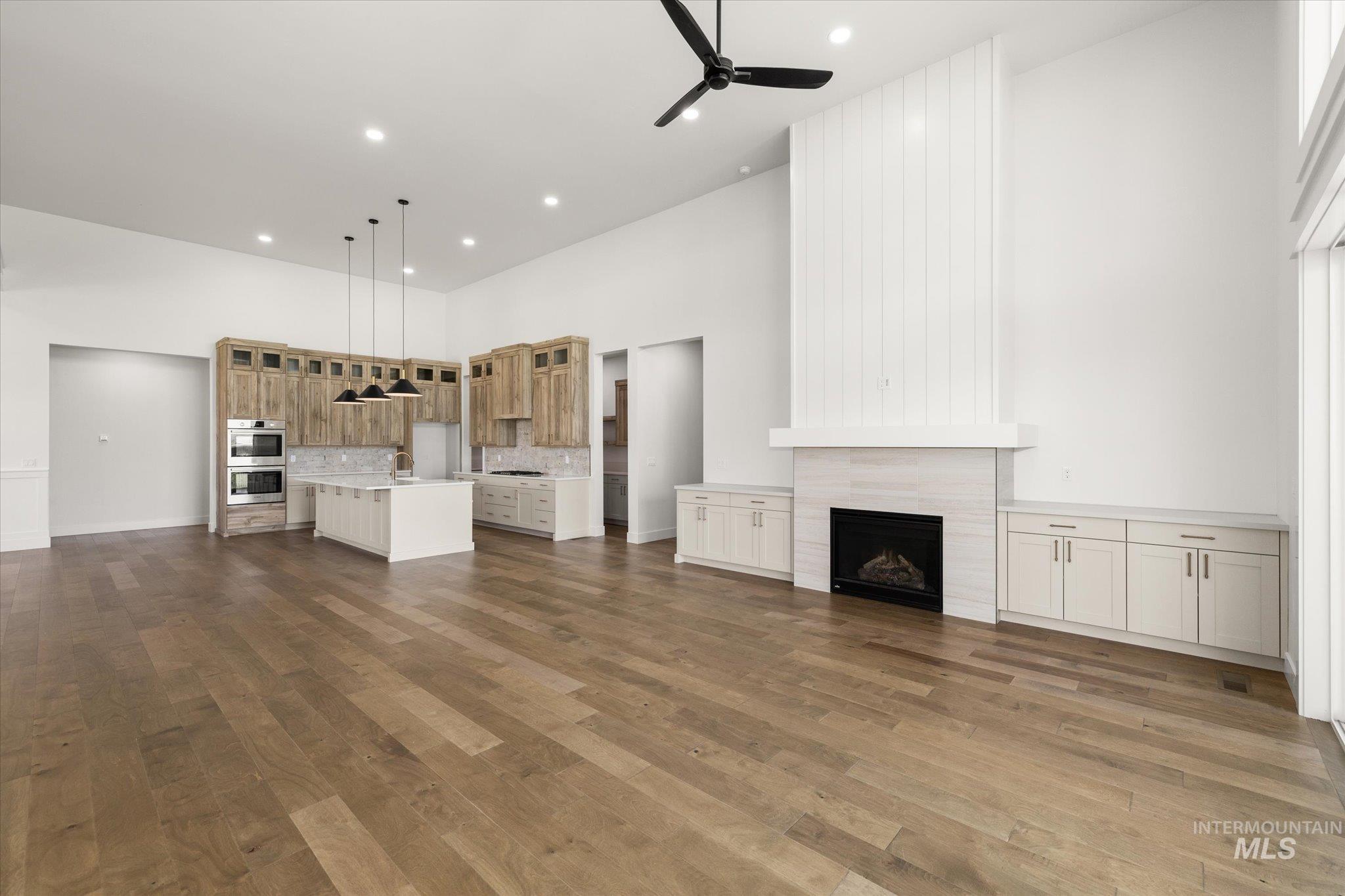 Unfurnished living room featuring a towering ceiling, a high end fireplace, a ceiling fan, dark wood finished floors, and recessed lighting