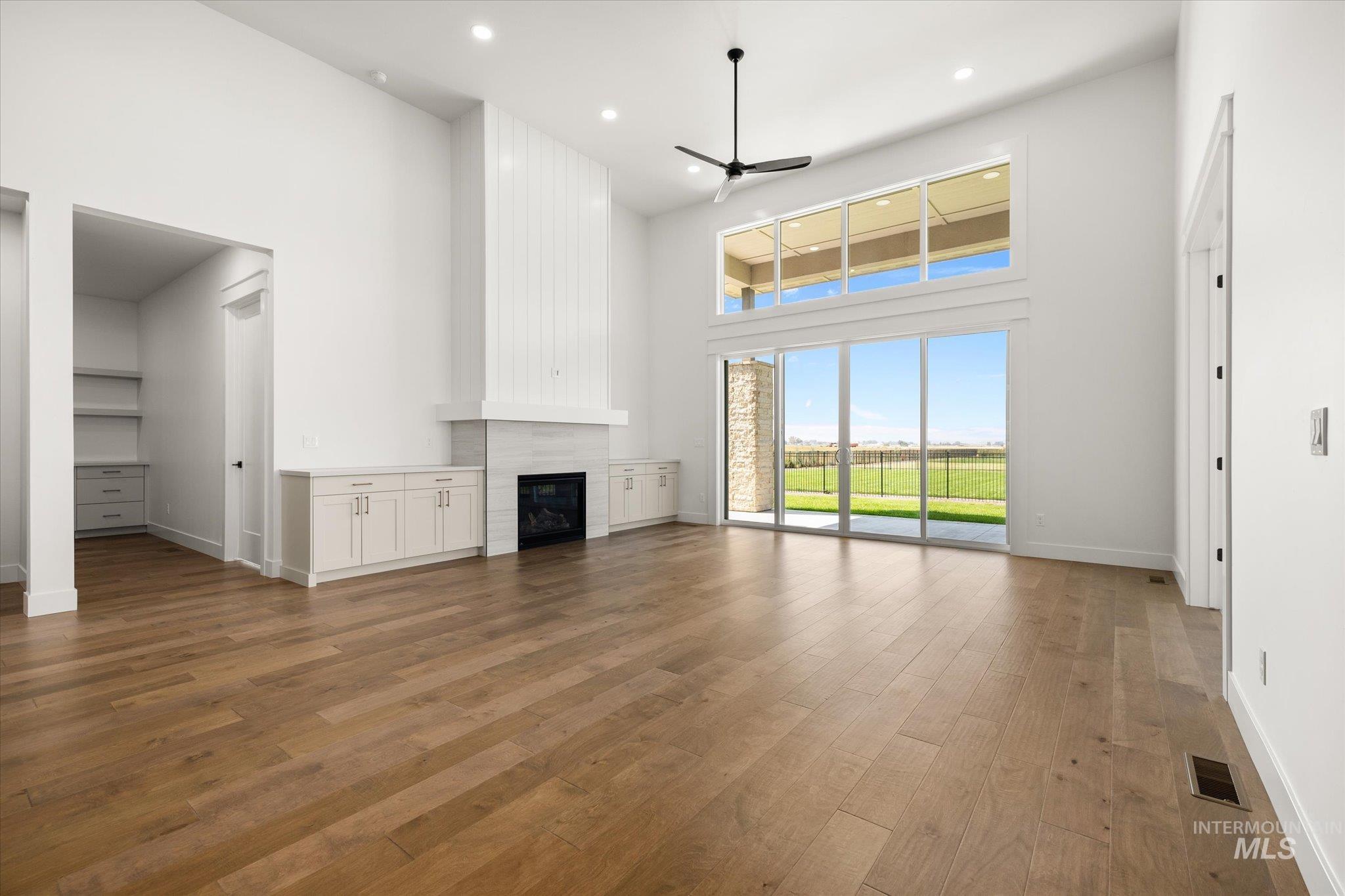 Unfurnished living room featuring a towering ceiling, ceiling fan, light wood-style flooring, a fireplace, and recessed lighting