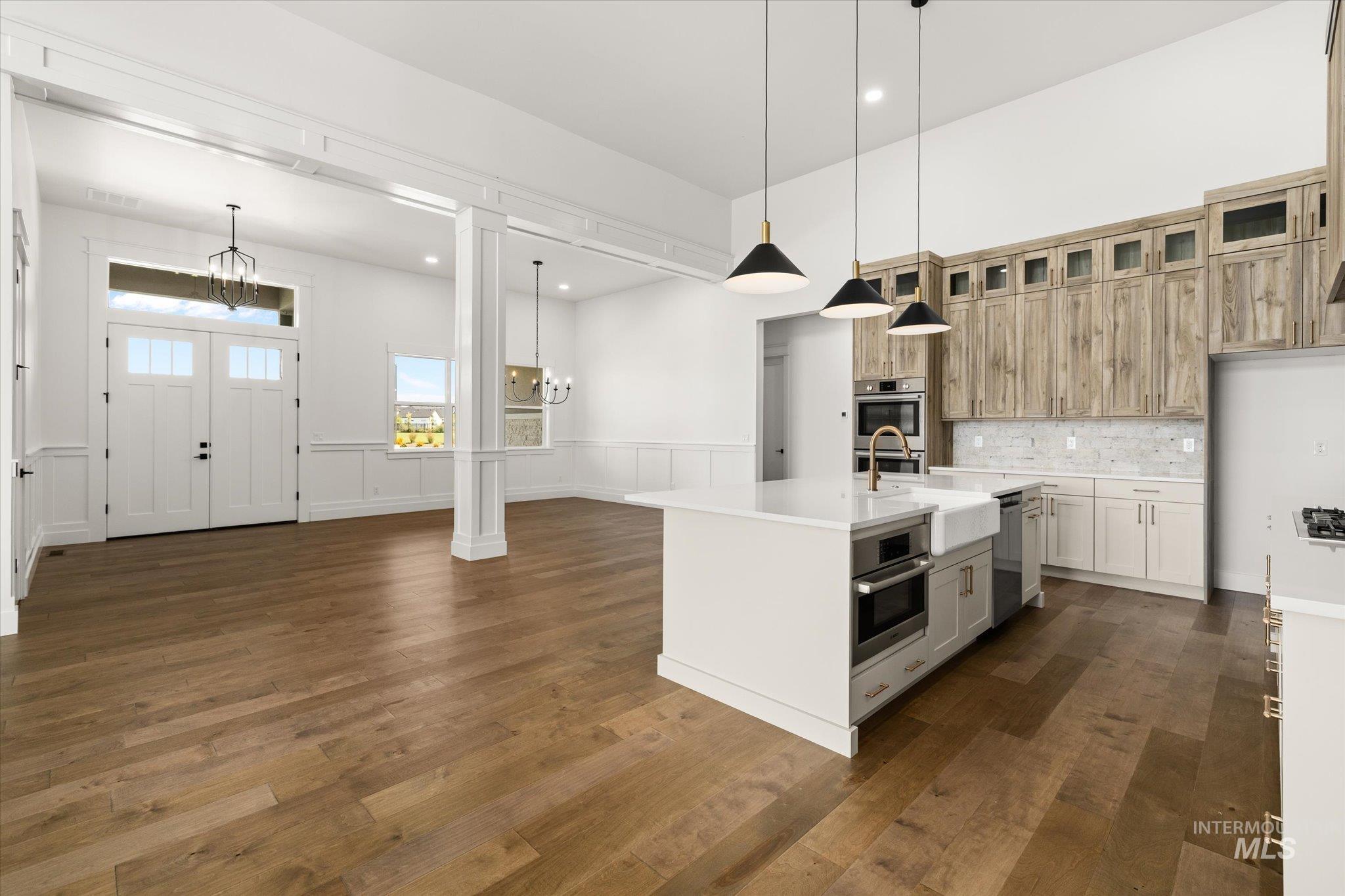 Kitchen with a center island with sink, dark wood-style floors, glass insert cabinets, open floor plan, and a wainscoted wall