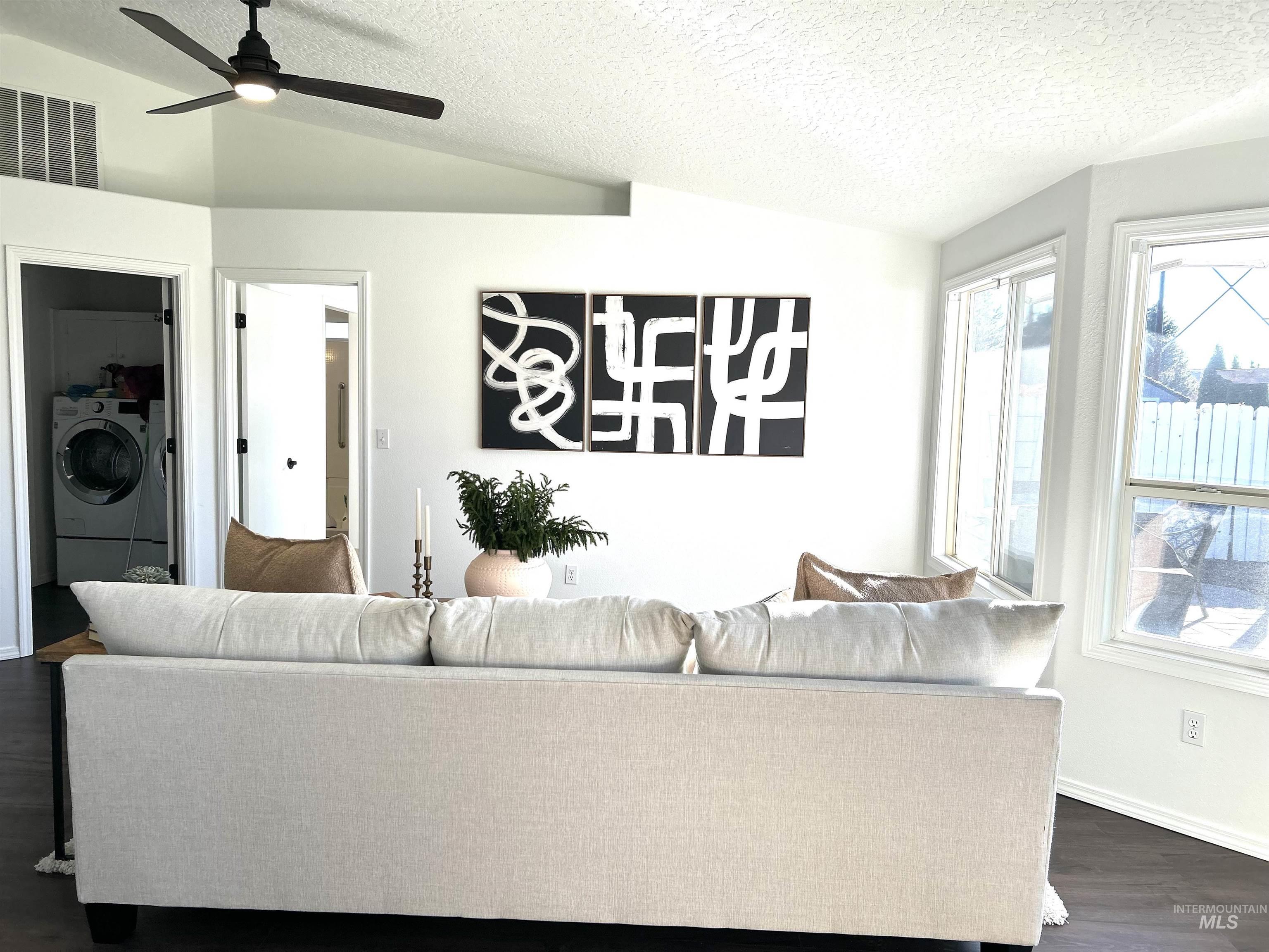 Living area featuring vaulted ceiling, dark wood-type flooring, a textured ceiling, and ceiling fan
