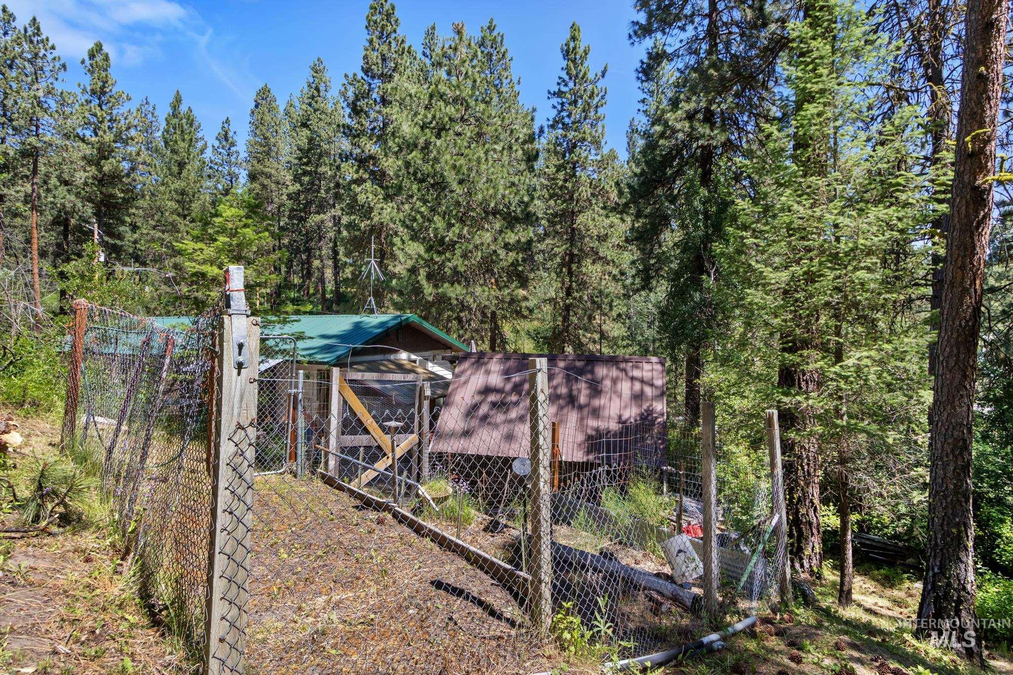 Fenced utility structure with a green metal roof, set amidst mature pine trees